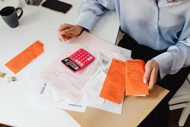 A woman reviews receipts and calculates expenses at a desk with a pink calculator. Periodiseringar och interimsposter i bokslutet